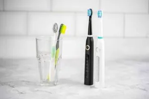 Are Electric Toothbrushes Better? - An image with two electric toothbrushes stood next to. a glass holding two manual toothbrushes